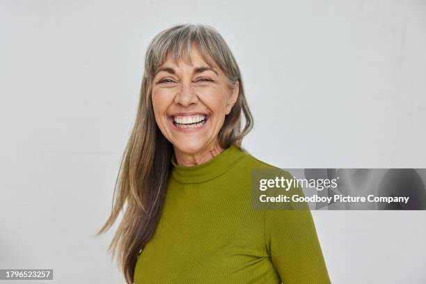unbekümmert reife frau lacht vor einem grauen hintergrund - zufriedenheit stock-fotos und bilder