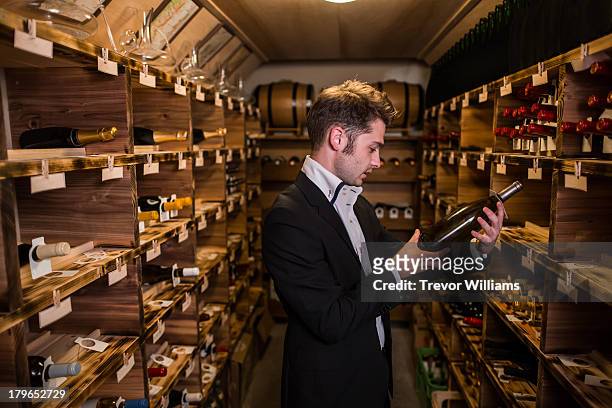 in a man in a wine cellar holding a bottle of wine - choosing wine stock pictures, royalty-free photos & images