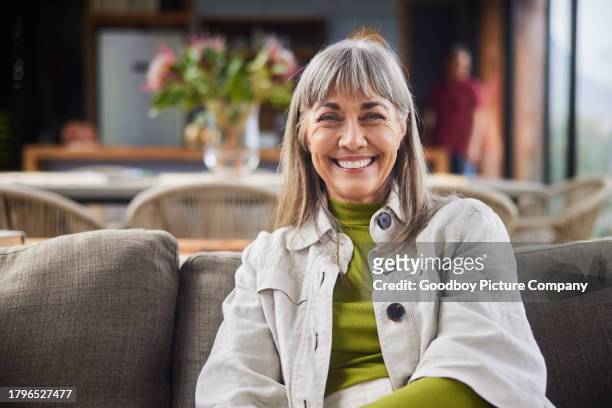 smiling mature woman sitting on her living room sofa - middle aged female active stock pictures, royalty-free photos & images