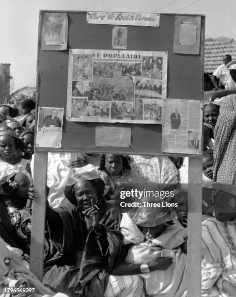 Group of people stand around a bulletin board with press cuttings, including a spread from French newspaper 'Le Populaire', beneath a sign reading...