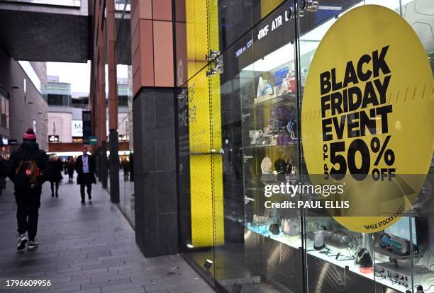 Pedestrians walk past a store with a Black Friday discount promotion in it's window, in Liverpool, north west England on November 22, 2023. Britain's...