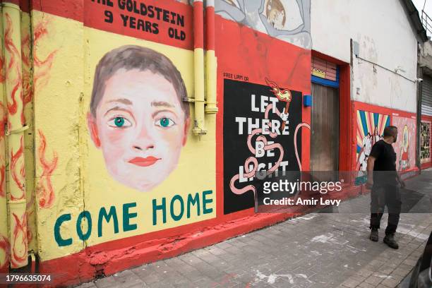 Man walks by wall paintings highlighting children held hostage in the Gaza Strip on November 22, 2023 in Tel Aviv, Israel. On Tuesday night, Israel...
