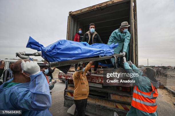 People carry the bodies of dead Palestinians, who lost their lives during the Israeli attacks, out of a truck to bury them in a mass grave in the...