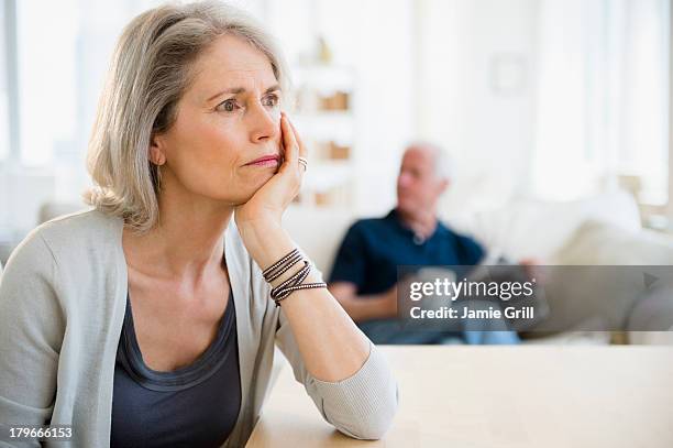 senior woman unhappy, husband in background - splitsen stockfoto's en -beelden