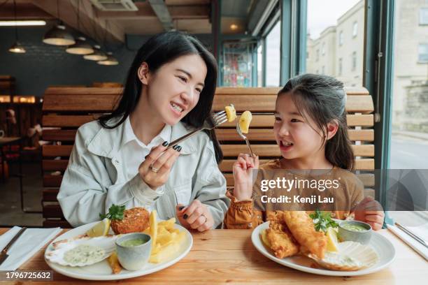 young asian mother and her daughter enjoying fish and chips in restaurant. having a fun time dining out with family. asian family enjoying a happy meal together. family eating out lifestyle. - girl eating fish stock pictures, royalty-free photos & images