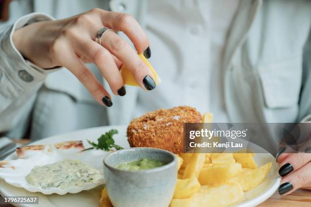 close up of young asian woman dripping lemon juice on fish and chips in restaurant. having a fun time dining out with family. asian family enjoying a happy meal together. family eating out lifestyle. - family eating potato chips imagens e fotografias de stock