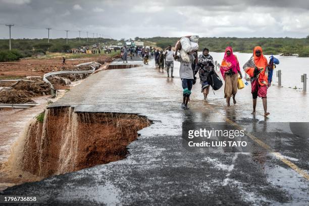 People carry their belongings while crossing the section of a road collapsing due to flash floods at the Mwingi-Garissa Road near Garissa on November...