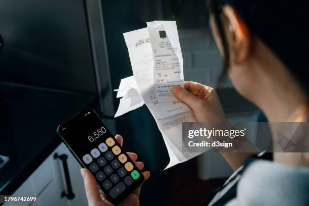 young asian woman calculating financial bills and receipts over kitchen counter, managing personal banking and finance. planning budget and calculating expenses at home. home budgeting. home finances concept - debiteuren stockfoto's en -beelden