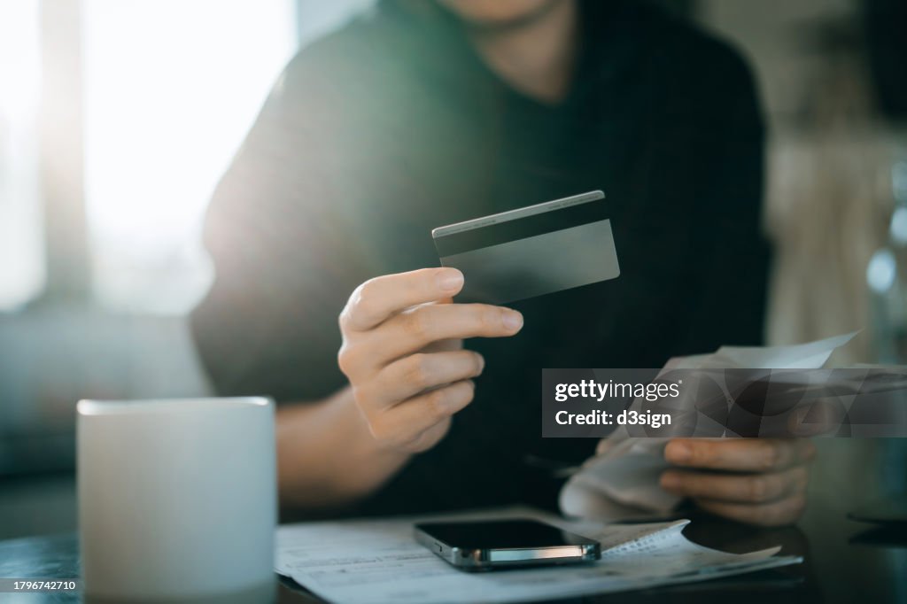 Cropped shot of young Asian woman holding credit card and expense receipts, handing personal banking and finance at home. Planning budget, calculating expenses and managing financial bills. Home budgeting. Home finances. Digital banking habits