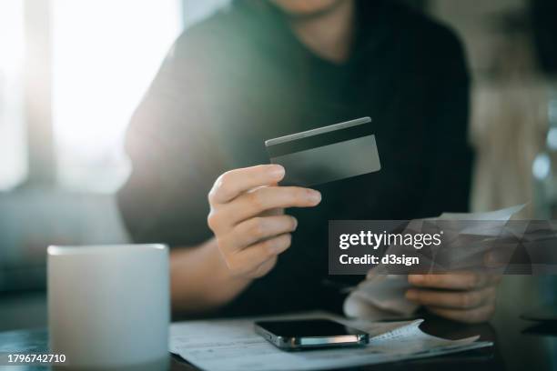 cropped shot of young asian woman holding credit card and expense receipts, handing personal banking and finance at home. planning budget, calculating expenses and managing financial bills. home budgeting. home finances. digital banking habits - debt fotografías e imágenes de stock