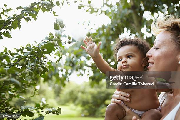 mother holding baby girl reaching for a leaf - linda rama fotografías e imágenes de stock