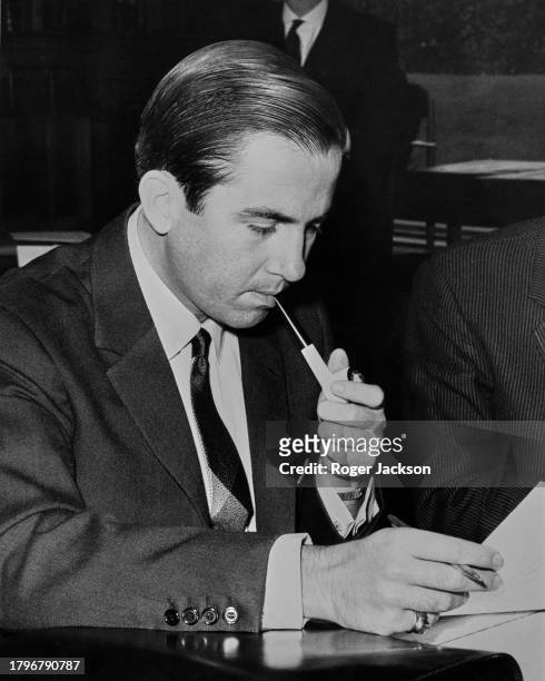 Greek Royal Constantine II of Greece smoking a pipe as he reads a document, a pen in his right hand, at the annual meeting of the Permanent Committee...