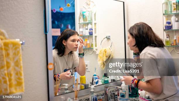 transgender non-binary teenager getting ready applying makeup in the mirror of a bathroom at home - transgender stockfoto's en -beelden