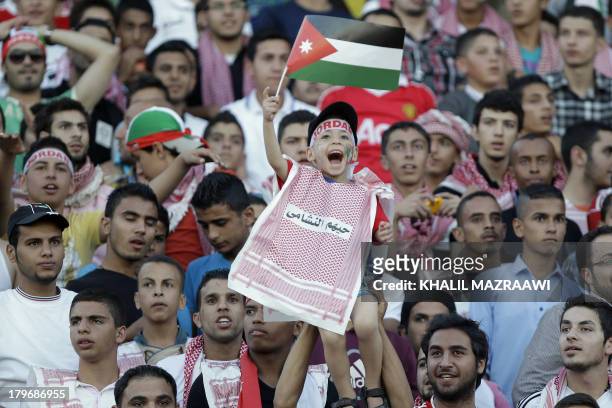 Jordanese boys waves his national flag and cheers as he watches his national team play their 2014 World Cup qualifier football match against...