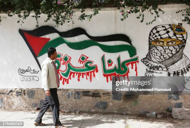 Yemeni man walks by a mural reading in Arabic "We all are Gaza", painted on a wall in solidarity with Palestinians and against the Israeli offensive...