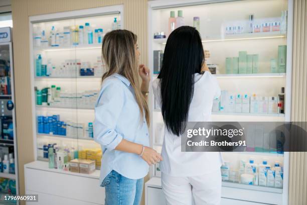 rückansicht einer apothekerin, die einem kunden im geschäft hilft - kosmetik beratung stock-fotos und bilder