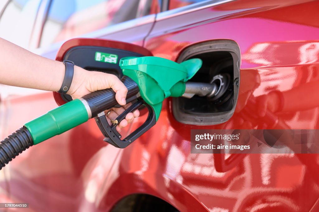 Close-up of a woman standing at a gas station filling her car with gasoline.