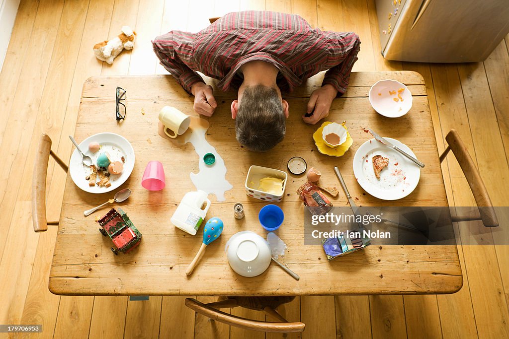 Overhead view of breakfast table with mature man amongst messy plates