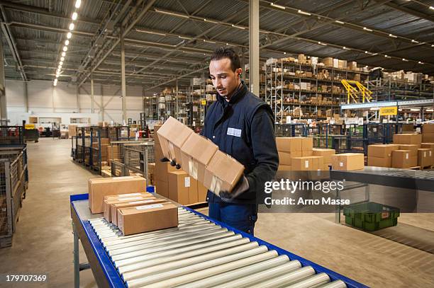 male warehouse worker selecting cardboard boxes from conveyor belt - boxes conveyor belt stock pictures, royalty-free photos & images