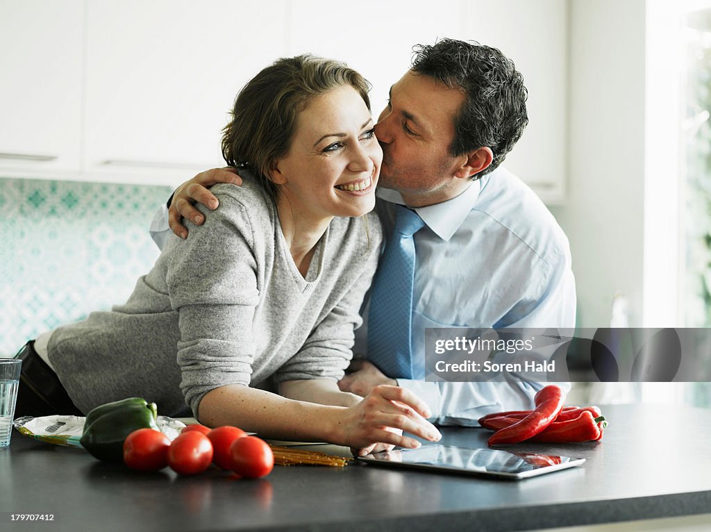 Businessman kissing wife in kitchen