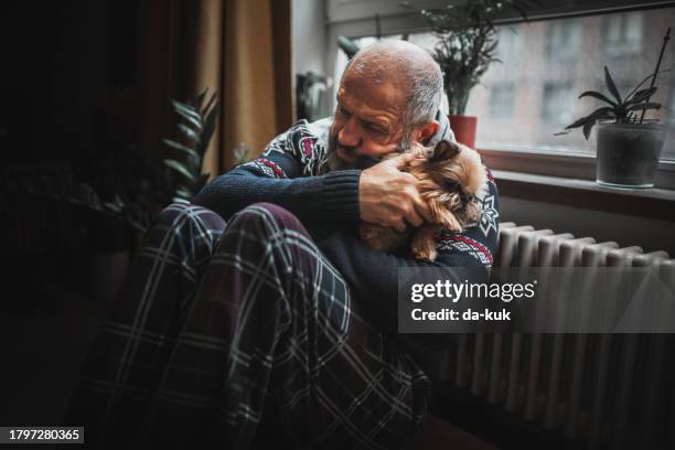 unwell man and his pet are cold in home. they’re trying to stay warm sitting next to the radiator. - pneumonia elderly stock pictures, royalty-free photos & images