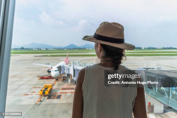 young woman looking at an airplane from inside the airport - hanoi airport stock pictures, royalty-free photos & images