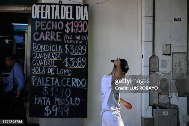 Man walks past a sign with a list of meat prices outside a butcher shop in Buenos Aires, on November 22, 2023.