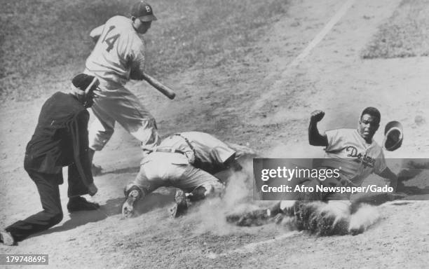 American baseball player Jackie Robinson of the Brooklyn Dodgers in action sliding past the other players towards home plate during a baseball game,...