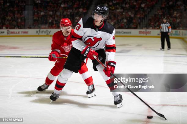 Luke Hughes of the New Jersey Devils skates up ice with the puck in front of Alex DeBrincat of the Detroit Red Wings during the second period at...