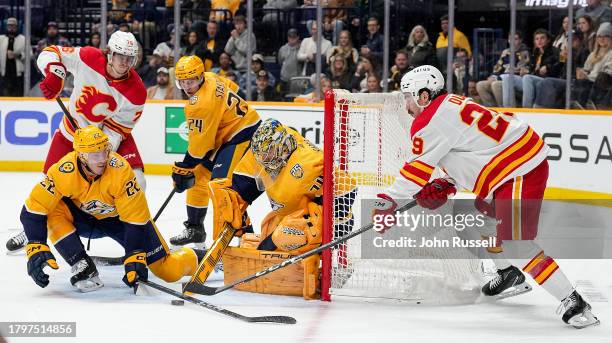 Tyson Barrie and Juuse Saros of the Nashville Predators defend against Dillon Dube of the Calgary Flames during an NHL game at Bridgestone Arena on...