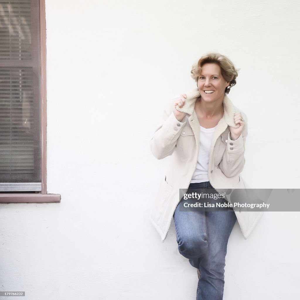 Woman in white jacket standing against white wall