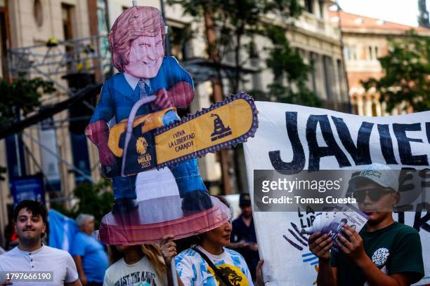 Supporters of Presidential candidate of La Libertad Avanza Javier Milei hold a sign depicting Milei wielding a chainsaw prior his closing rally ahead...