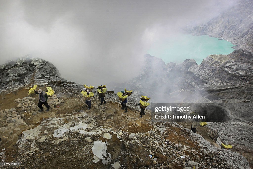 Miners carry sulfur blocks up rocky volcano cliff