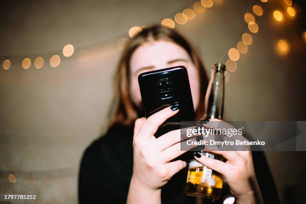 young woman using smart phone while having beer at party - dronken stockfoto's en -beelden