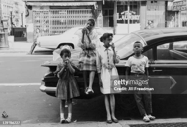 Group of children lean against a car to eat candy, New York City, 1966.