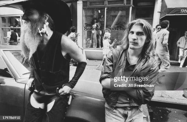 Two men, one with a tap in his earlobe, lean against a car in Greenwich Village, New York City, 1979.