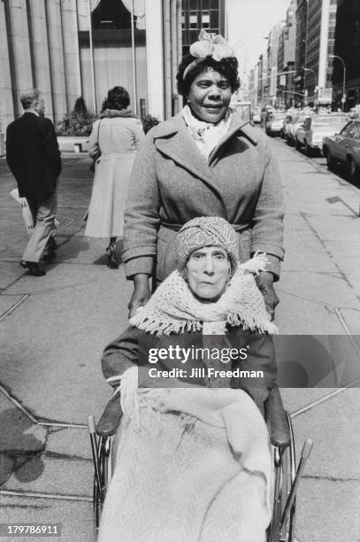 Woman pushes an elderly woman in a wheelchair in Midtown Manhattan, New York City, 1982.