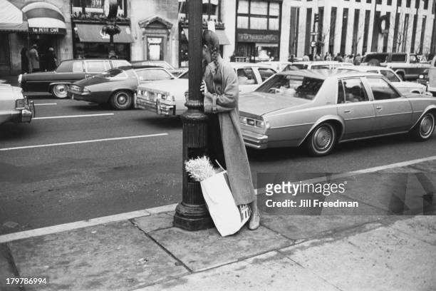 Woman with a shopping bag leans against a lamppost on 5th Avenue and 59th Street, New York City, 1979.