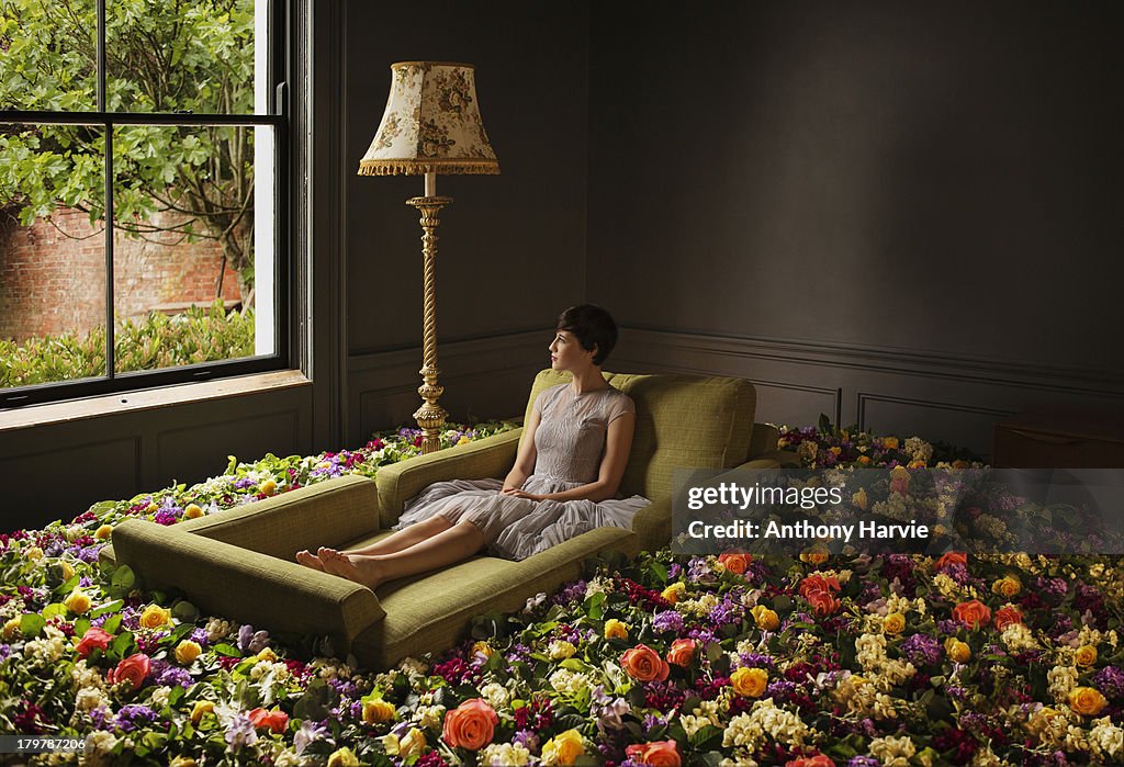 Woman sitting on sofa surrounded by flowers