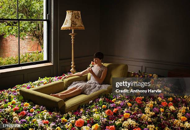 woman sitting on sofa surrounded by flowers - enjoyment photos stock pictures, royalty-free photos & images