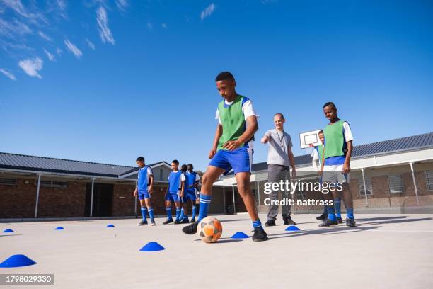 los colegiales practican sus habilidades futbolísticas en el patio con su entrenador - entrenamiento deportivo fotografías e imágenes de stock