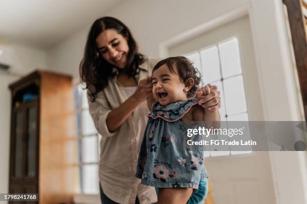 mother supporting her daughter to take the first steps in the playroom - life events stock pictures, royalty-free photos & images
