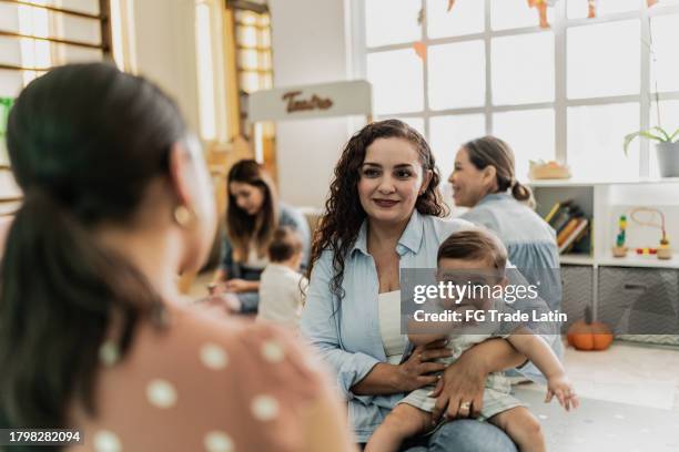 mother talking while holding her son in a support group at playroom - nursery school building stock pictures, royalty-free photos & images