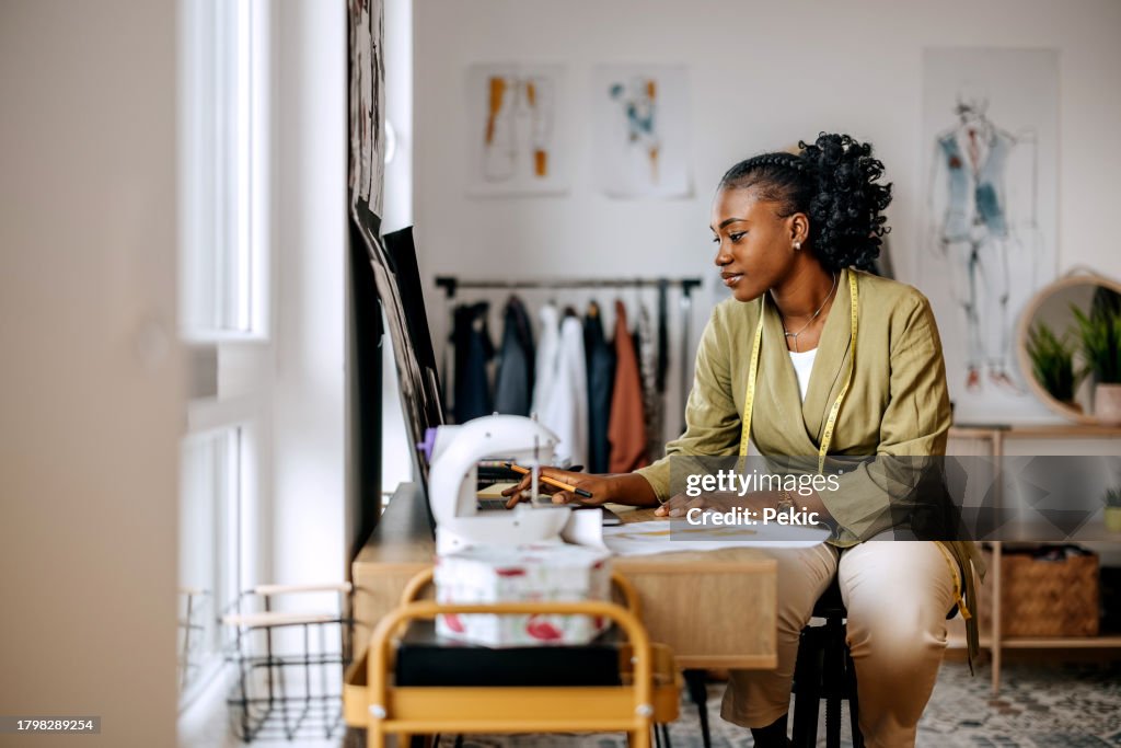 Junge schöne weibliche Bekleidungsdesignerin zeichnet Skizzen in der Werkstatt