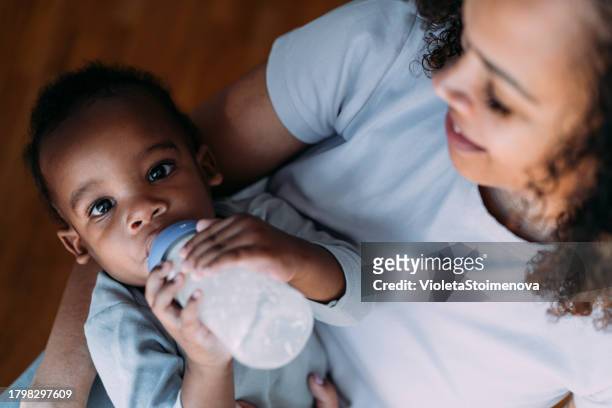 une mère nourrit son petit garçon avec du lait pour bébé. - milk bottle photos et images de collection