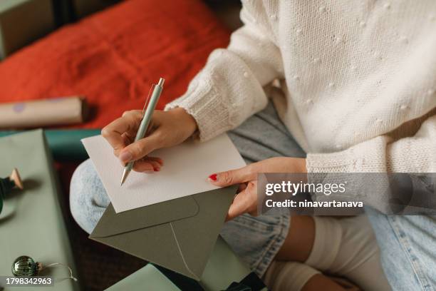 close-up of a woman sitting cross-legged on the floor next to a wrapped christmas gift writing a christmas card - christmas card stockfoto's en -beelden
