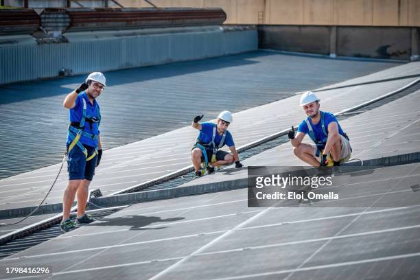 großartige teams, die zwischen solarmodulen auf dem dach eines fabrikgebäudes arbeiten - ok werk stock-fotos und bilder