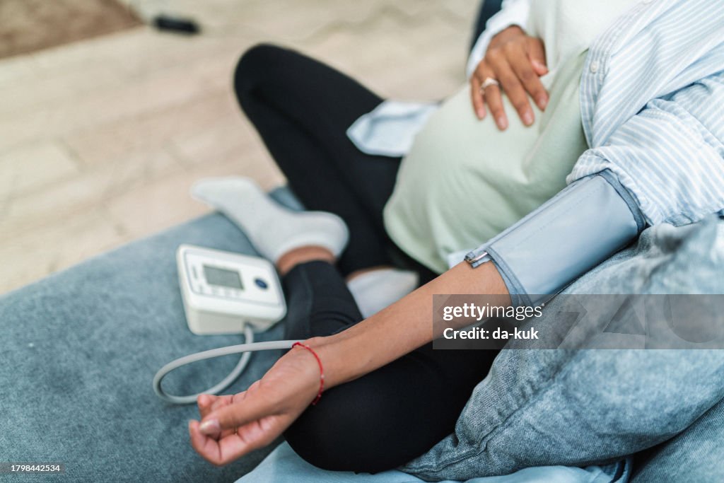 Young pregnant woman measures her blood pressure with a digital meter