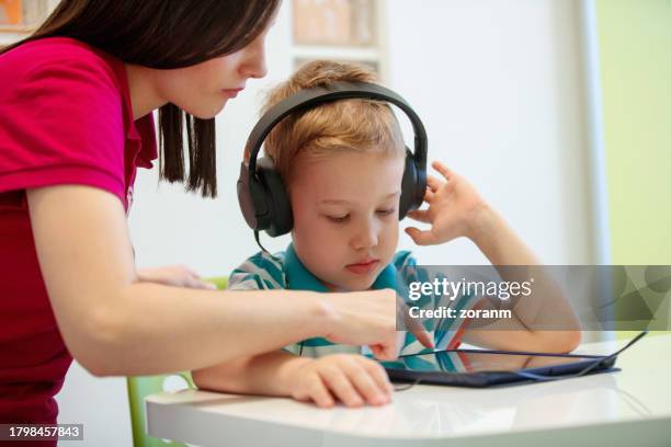little blond boy with headphones using tablet assisted by audiometrist at session - assistive technology stock pictures, royalty-free photos & images