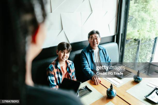 father and son talking and ordering to waitress at asian restaurant - family ordering at restaurant stock pictures, royalty-free photos & images